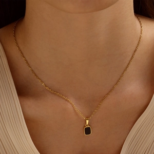 Golden necklace featuring a black rectangular pendant with beaded edges on a model