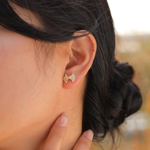 Vue macro de boucles d'oreilles nœud dorées avec zircons portées par un mannequin