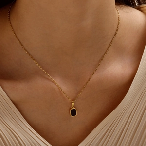 Close-up of golden necklace featuring a black rectangular pendant with beaded metal edges