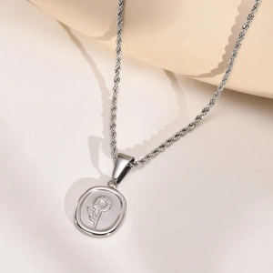 Détail macro du pendentif tournesol argenté et chaîne torsadée sur fond crème minimal