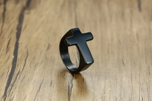 Detailed view of black matte stainless steel ring with a bold 3D cross on wood surface