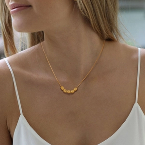 Macro detail of minimalist gold snake chain necklace with five polished oval beads