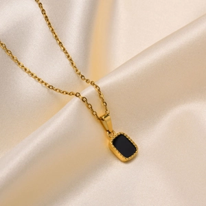 Close-up of minimalist gold pendant necklace featuring a black rectangle stone on champagne silk