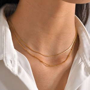 Close-up of double layer gold snake chain and beaded necklace on woman in white shirt