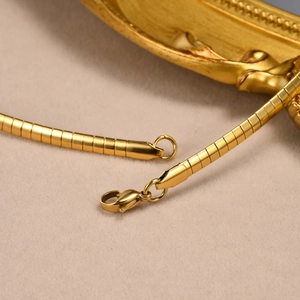 Detailed close-up of golden flat snake chain necklace with lobster clasp on beige velvet