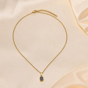 Elegant gold chain necklace with black rectangular pendant on silk fabric background