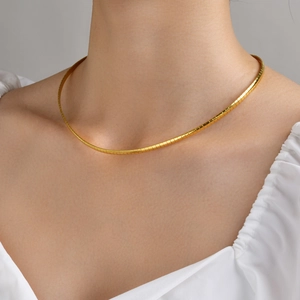 Detail of a thin gold flat snake chain necklace worn on a woman's neck for a luxury look