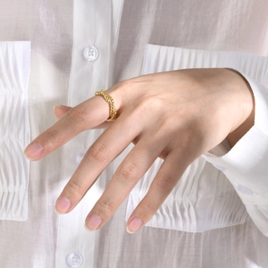 Detailed view of a gold-plated twisted band ring worn on a finger with a soft fabric background