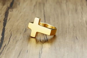 Detailed macro view of a gold-finished stainless steel cross ring on wood surface