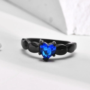 Close-up of black plated ring with heart-shaped blue zircon on white geometric stone