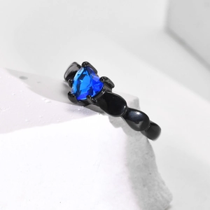 Detail of a black beaded band ring with a heart-shaped blue zircon stone on white marble