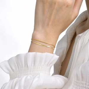 Elegant 18K gold-plated double snake chain bracelet set on woman's wrist with white cuff