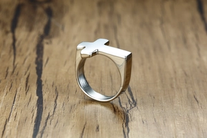 Macro shot of silver stainless steel cross ring with a polished finish on wood texture