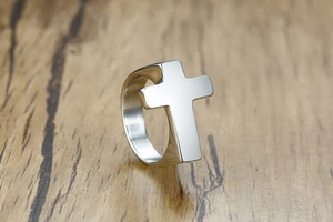 Polished silver cross ring detail with a mirror finish on a natural wood surface