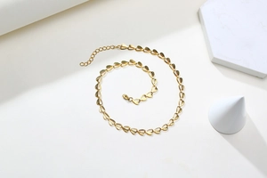 Close-up of golden leaf chain necklace with lobster clasp and extension chain on white marble