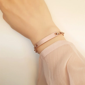 Dettaglio di un bracciale a barra in oro rosa lucido con catena minimalista al polso