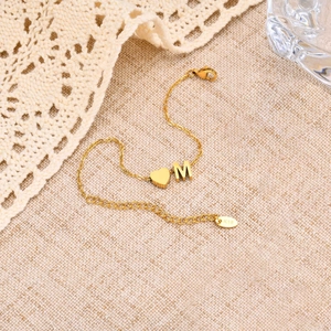 Détail du bracelet doré avec lettre M et cœur, incluant la gravure K18 sur la chaîne