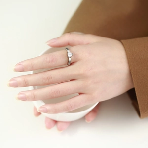 Detail of hollow heart-shaped silver ring with central heart-cut zircon on finger