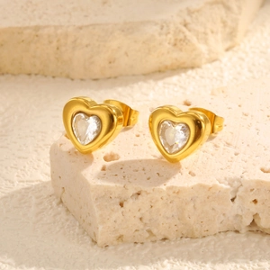 Macro detail of gold heart earrings with clear cubic zirconia on stone texture