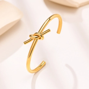 Macro detail of a knotted gold cuff bracelet featuring a polished mirror-like finish
