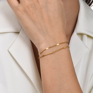Close-up of golden double-layered bracelet with rectangular metal charms on wrist