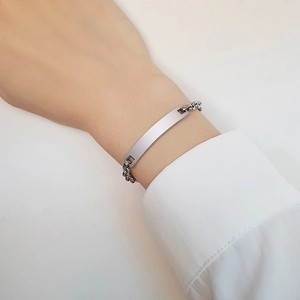 Dettaglio di un bracciale ID in argento lucido con barra curva e catena a maglia grumetta