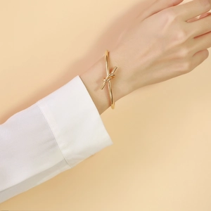 Minimalist gold knotted stainless steel open bangle bracelet shown on a female wrist