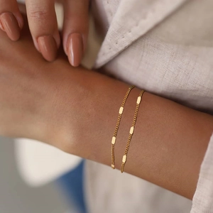 Detail of a thin gold layered chain bracelet with rectangular charms on a model's wrist