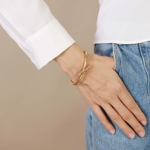 Elegant gold-tone knot cuff bracelet for women, minimalist open design on model's wrist