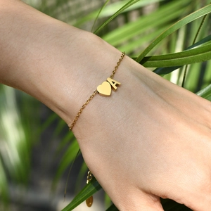 Détail du bracelet en acier inoxydable doré avec lettre A et breloque cœur au poignet