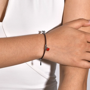 Close-up of a red heart charm and silver beads on a minimalist black cord bracelet