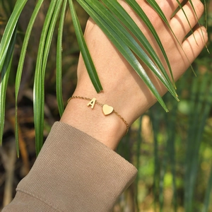 Détail d'un bracelet en acier doré avec lettre A et breloque cœur porté au poignet