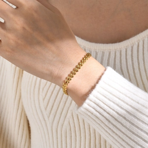 Close-up of a golden wheat chain bracelet worn on a wrist with a white sweater background