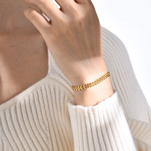 Detail of a golden wheat chain bracelet on wrist showing heart shaped link texture