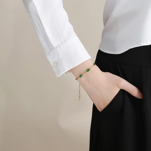 Detail of a gold bracelet with emerald green zircon stones on a female wrist