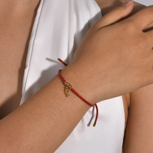 Detail of red braided bracelet with golden dolphin charm and beads on a woman's wrist