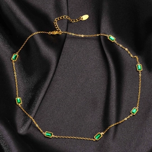 Detail of gold necklace with rectangular emerald zircons on black silk background
