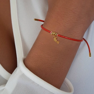 Close-up of a red cord bracelet featuring gold dolphin charm and metallic beads