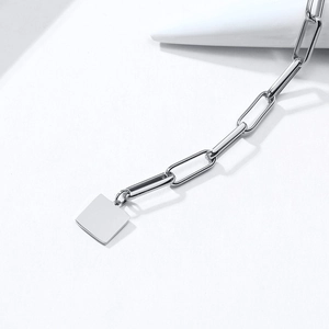 Détail d'un bracelet chaîne trombone argenté orné d'un pendentif carré en métal poli
