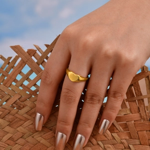 Gros plan d'une bague chevalière coeur en or 18 carats portée par un mannequin au soleil