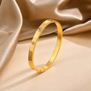 Dettaglio di un bracciale dorato in acciaio con zirconi quadrati su tessuto di seta
