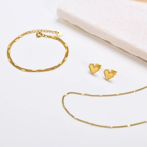 Golden double-layer chain necklace and bracelet set with heart stud earrings on stone