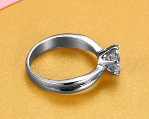 Side view of silver six-prong crown ring with round sparkling gemstone on orange background
