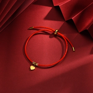 Close-up of red leather adjustable bracelet with gold heart charm on crimson background