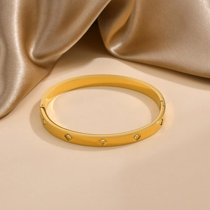 Dettaglio del bracciale in acciaio dorato con zirconi quadrati su tessuto di raso