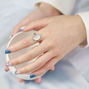 Close-up of a minimalist silver oval ring on model hand with blue floral nail art