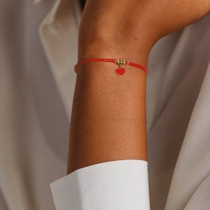 Macro shot of red braided adjustable bracelet featuring heart charm and gold beads