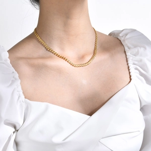 Close-up of a golden wheat chain necklace worn by a model for minimalist styling