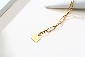 Gros plan d'un bracelet maille trombone doré avec un pendentif carré sur fond blanc