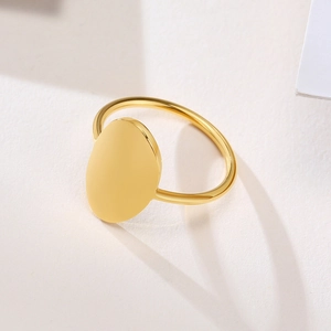 Close-up of minimalist gold stainless steel oval signet ring on white textured surface